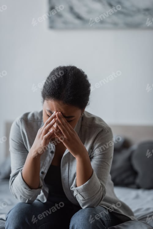 Preview: Depressed multiracial woman crying on blurred bed at home