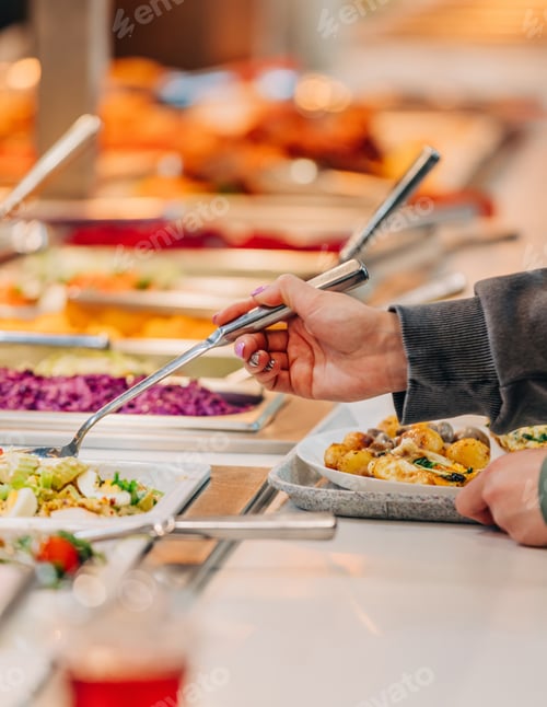 Preview: woman puts food on her plate at the buffet, closeup view