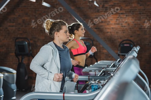 Preview: Sporty and overweight women training on treadmills at gym