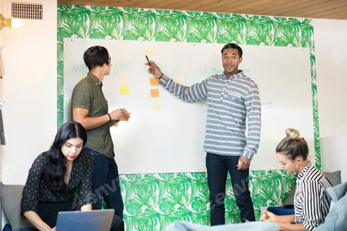 Preview: Young businessman pointing at whiteboard in creative meeting room