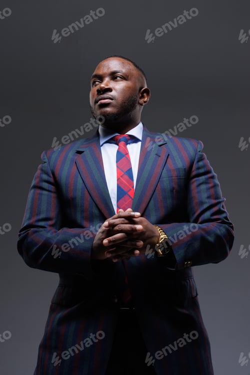 Preview: Confident businessman in a stylish striped suit and tie, posing with hands clasped