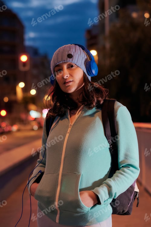 Preview: Serious young woman with headphones looking at camera at night