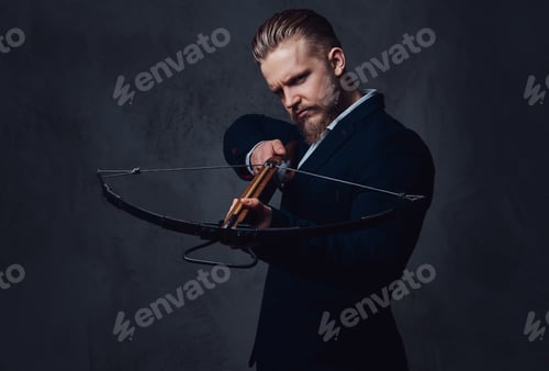 Preview: A man dressed in a suit holds crossbow.