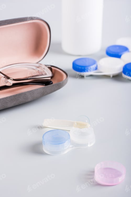 Preview: Contact lens on an open storage container on the background of a case with glasses. Vertical view