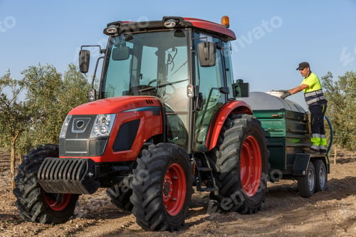 Preview: Tractor spraying fertilizer in olive grove by farmer during sunny day
