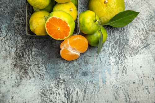 Preview: Half shot of a basket with fresh green tangerines cut in half and peeled tangerine on gray