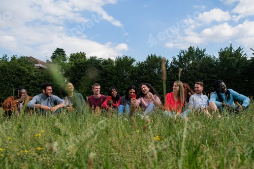 Preview: Group of friends from different cultures sitting on the meadow lifestyle outdoors