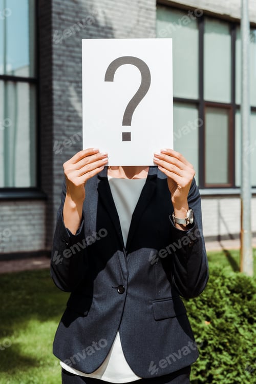 Preview: cropped view of woman holding placard with question mark near building