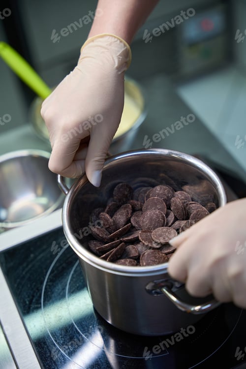 Preview: Woman confectioner placing bowl of chocolate chips over pan of simmering water