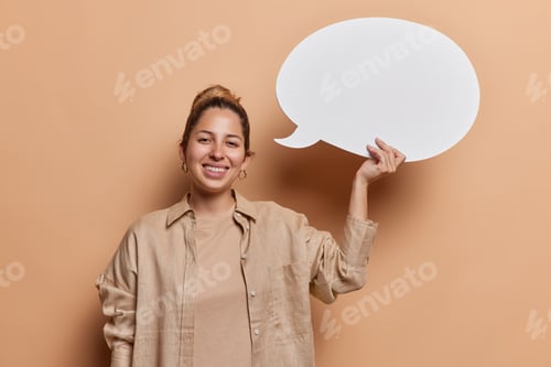 Preview: Horizontal shot of pretty pleased young woman with hair bun dressed in casual shirt holds blank