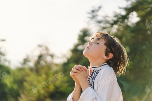 Preview: A young child wearing a traditional embroidered shirt quietly prays outdoors