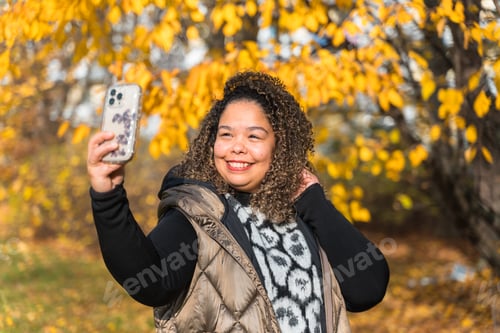 Preview: Happy brazilian woman taking selfie in autumn park