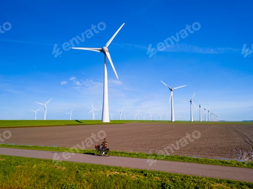 Preview: A man rides his electric bicycle down a dirt road alongside towering wind turbines on a sunny day in