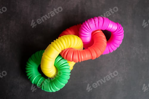 Preview: kids anti stress sensory pop tube plastic fidget push toy on a black table or floor. flat lay