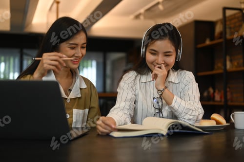 Preview: Two cheerful young students reading book while preparing for exams in college library. E