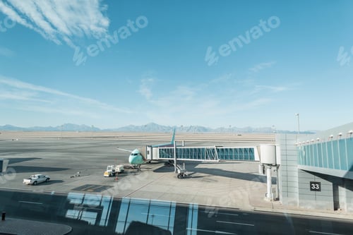 Preview: Beautiful plane with a landing bridge at the airport on a background of mountains, desert