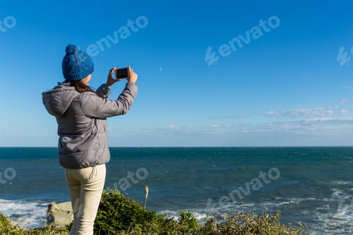 Preview: Woman take photo on cellphone at the seaside in winter time
