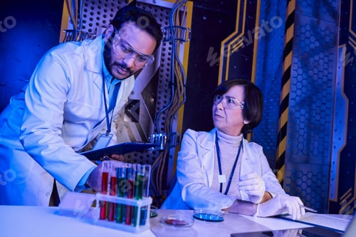 Preview: indian scientist looking at test tubes with alien life samples near colleague in neon-lit lab