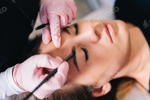 Preview: Beautician styling eyebrow shape and design on her client's face in a beauty salon