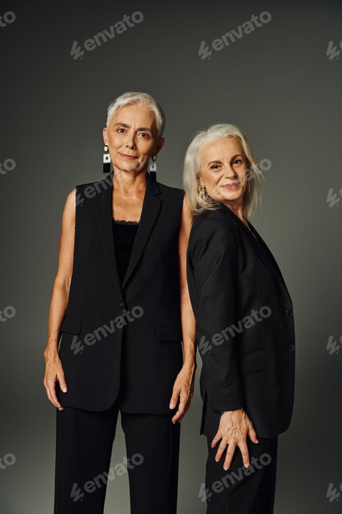 Preview: positive mature models in black classic attire smiling at camera on grey, timeless elegance