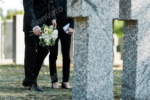 Preview: cropped view of man standing near woman with flowers near tombs