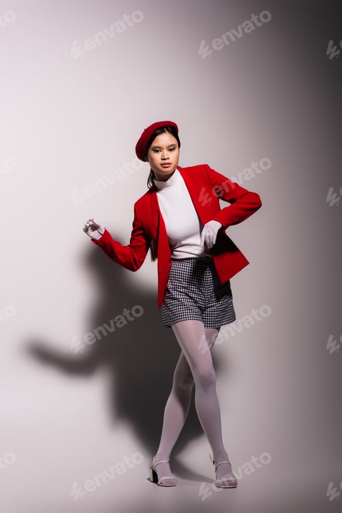 Preview: Trendy asian model in white gloves and red jacket posing on grey background with shadow