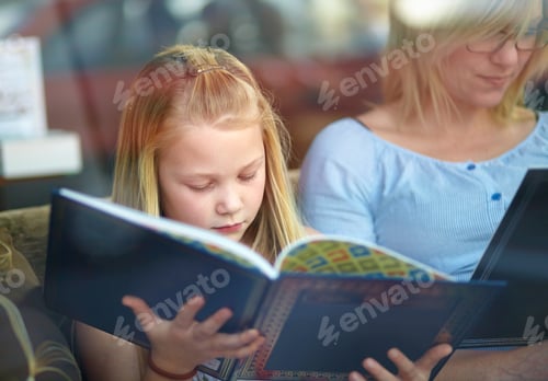 Preview: Reading exercises the brain. A cute young girl sitting next to her mother while they read a book.