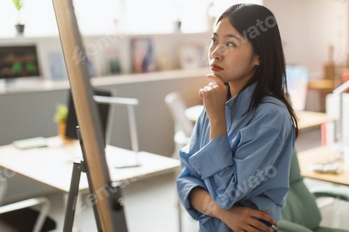 Preview: Thoughtful Asian Businesswoman Looking At Whiteboard In Modern Office