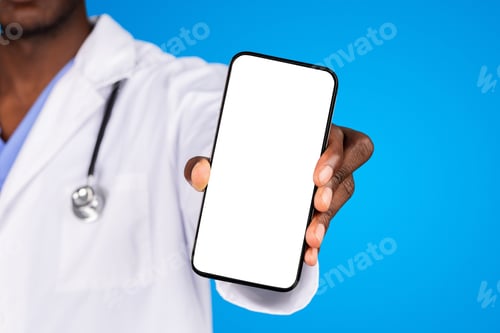 Preview: Millennial african american doctor in white coat show smartphone with blank screen