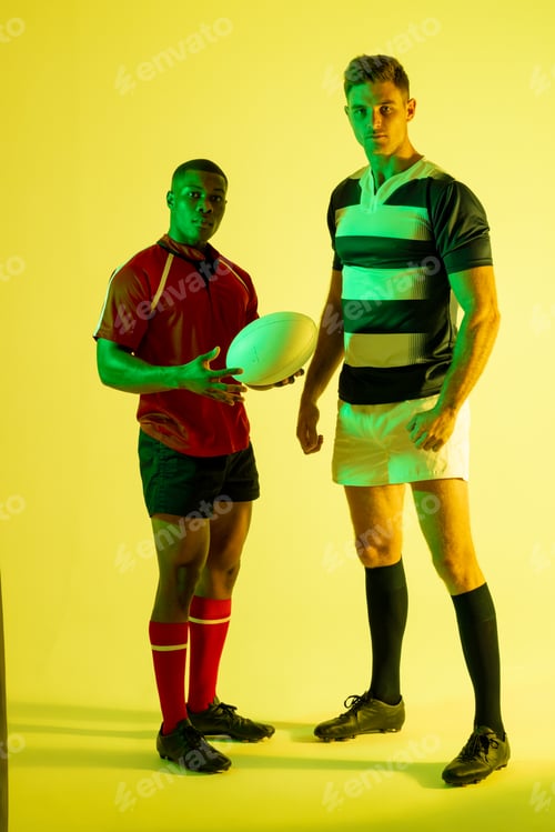 Preview: Portrait of diverse male rugby players with rugby ball over yellow lighting