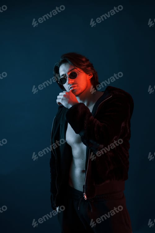Preview: Beautiful man in glasses and black clothes is in the studio with blue neon lighting