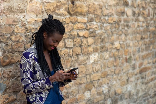 Preview: African-American woman with curly hair browsing phone in street