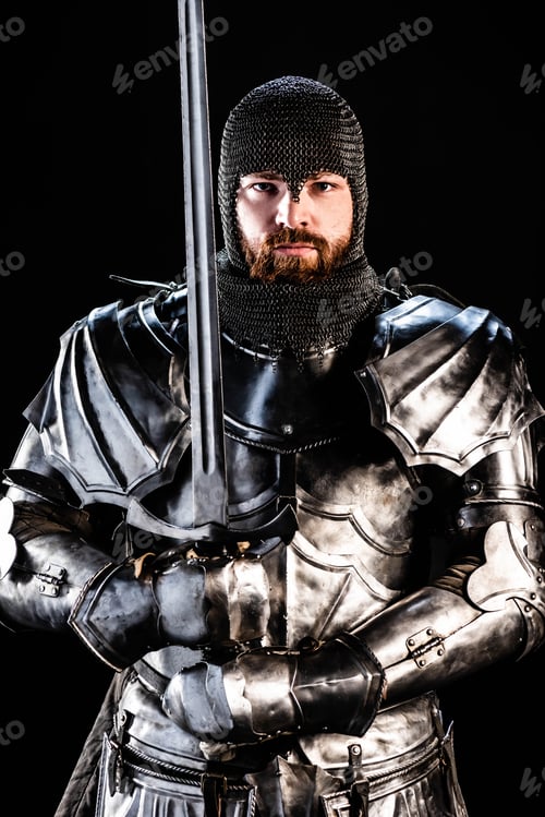 Preview: handsome knight in armor looking at camera and holding sword isolated on black