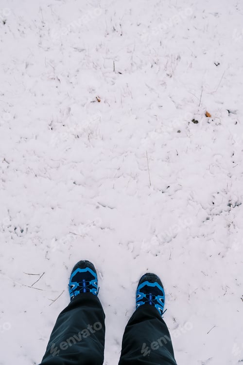 Preview: Feet in blue trekking boots stand on the snow. Top view