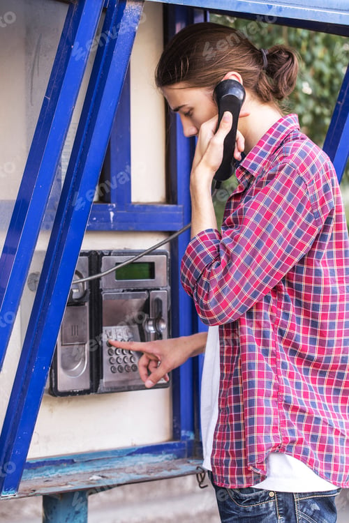 Preview: Young man dialing number on public phone.
