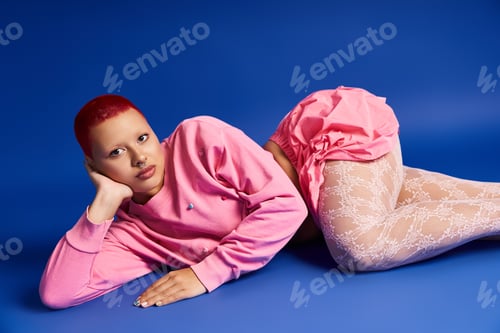 Preview: Young woman with bright pink hair poses confidently against a bold blue backdrop