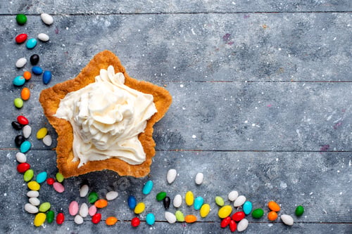Preview: top view little yummy cake with cream and different colorful candies all over the light background