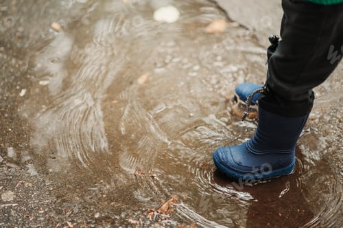 Preview: Boy feet in rubber boots while playing outside on a rainy day