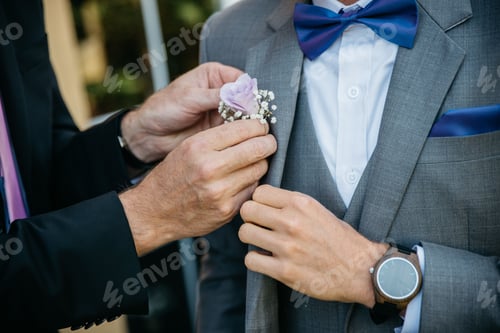 Preview: Closeup shot of a groomsman helping the groom putting the flower in his jacket