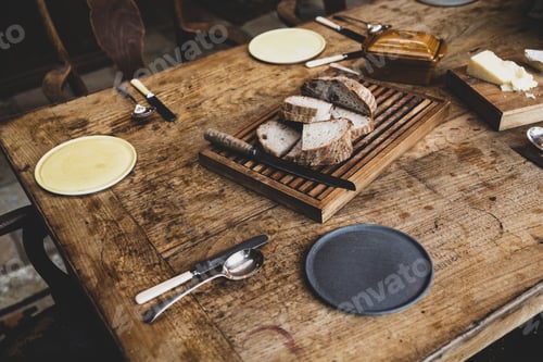 Preview: High angle close up of plates, cutlery and bread on a vintage wooden table.