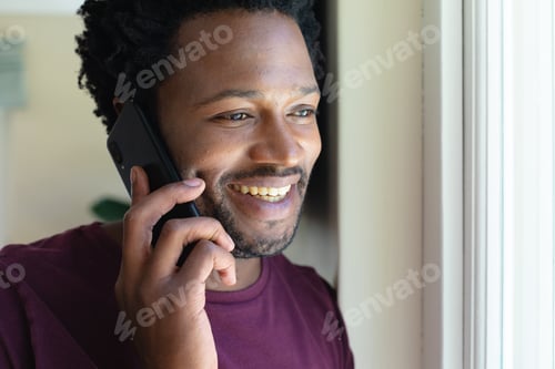 Preview: Smiling young african american man talking on mobile phone at home