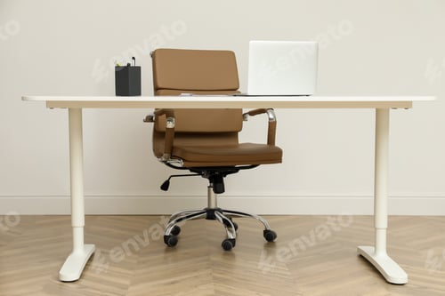 Preview: Stylish workplace with laptop and comfortable armchair near white wall indoors. Interior design