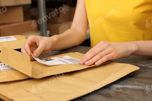 Preview: Post office worker sticking barcode on parcel at counter indoors, closeup
