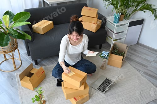 Preview: Overhead view small business owner packing product in cardboard box for delivery to customers.