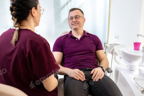 Preview: Patient sits in dental chair while talking to dentist in modern clinic