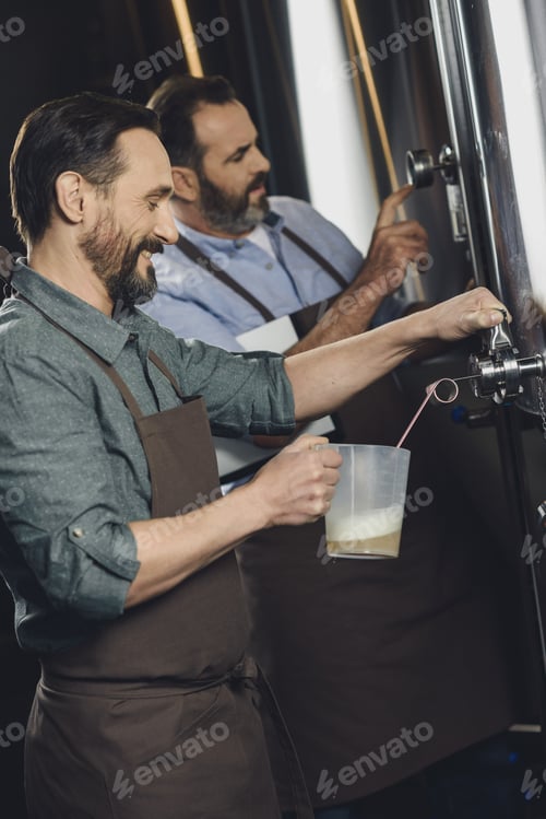 Preview: Male brewery worker pouring beer from the tank to plastic pitcher