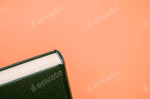 Preview: Top view closeup of an ancient book with a dark green cover isolated on an orange background
