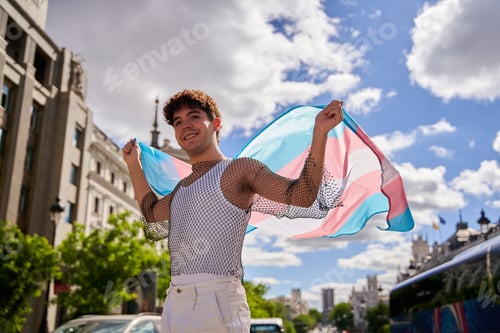 Preview: Transman raising the transgender flag outdoors.