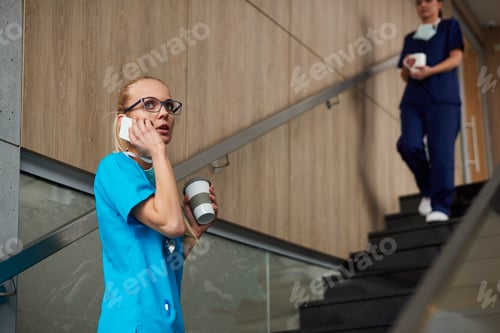 Preview: Surgeon using smartphone, holding coffee cup, colleague walking down stairs in background