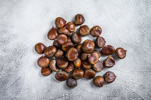 Preview: Raw chestnuts on a wooden table. White background. Top view